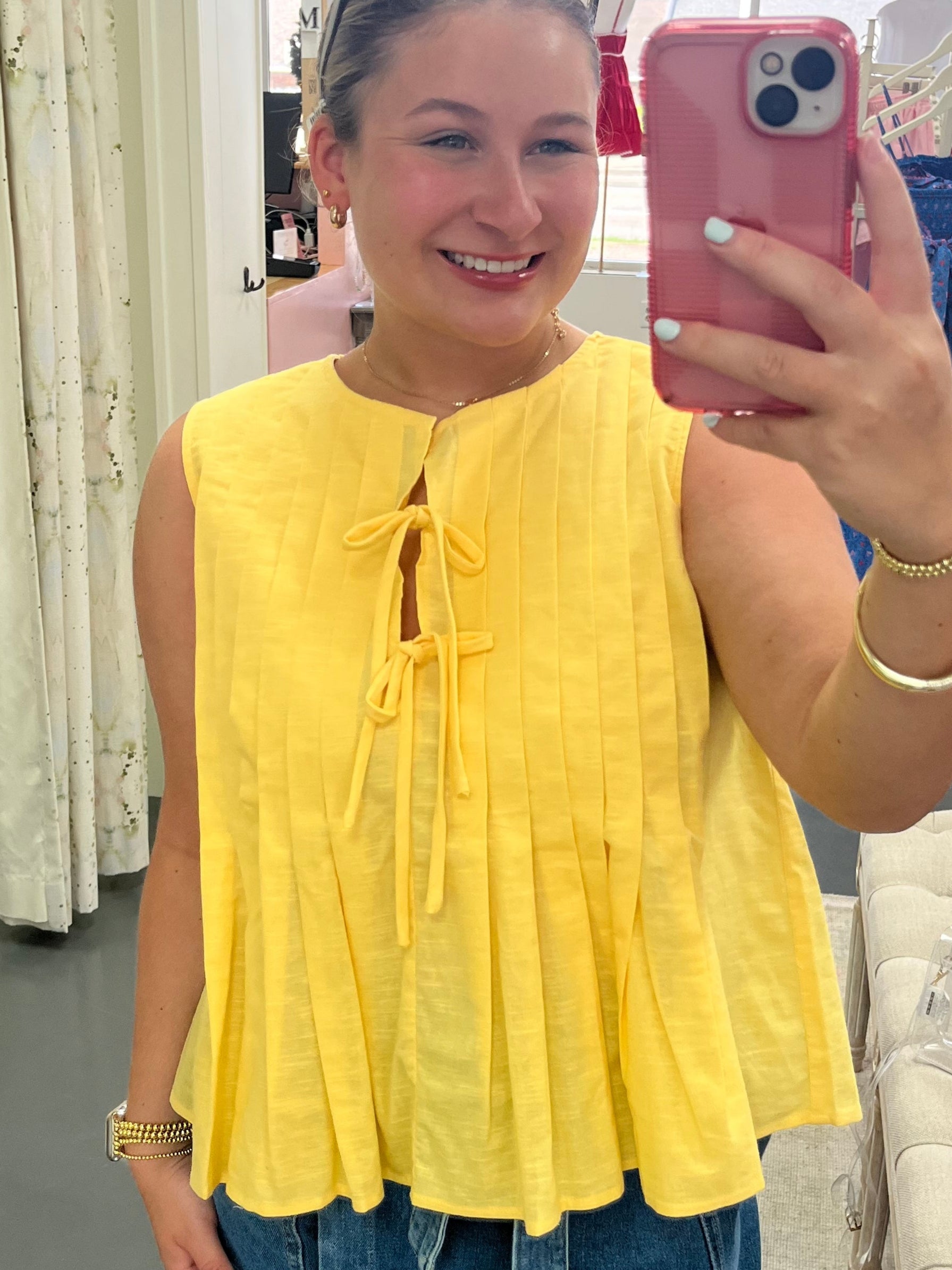 Person wearing a yellow top and denim shorts taking a mirror selfie.