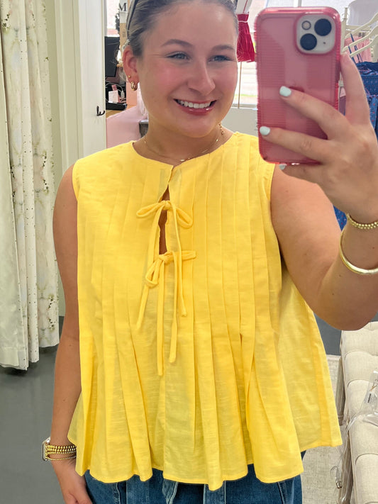 Person wearing a yellow top and denim shorts taking a mirror selfie.